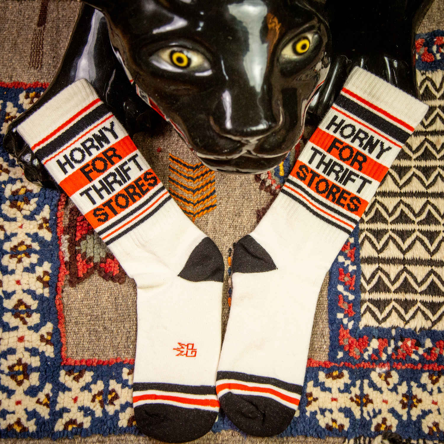 A pair of off-white and red crew socks that read "horny for thrift stores" with the Gumball Poodle logo on the arch.