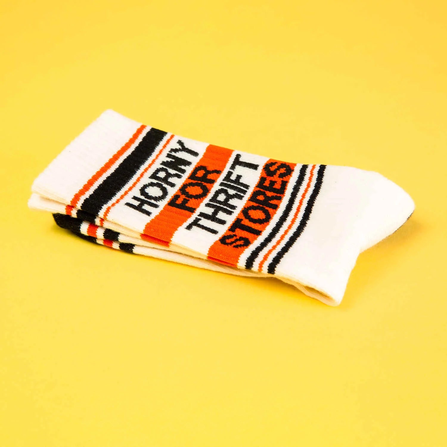 A pair of off-white and red crew socks that read "horny for thrift stores" with the Gumball Poodle logo on the arch.