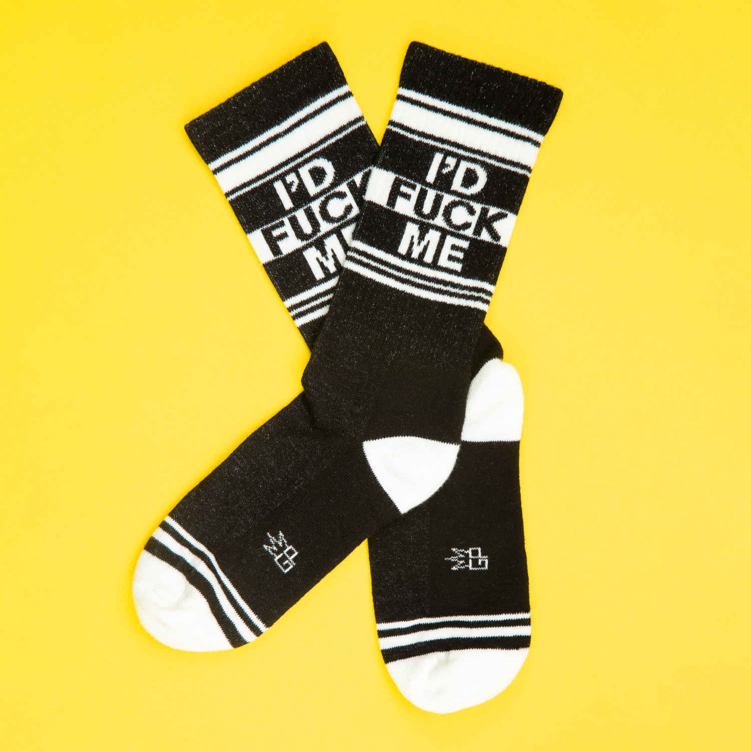 A pair of black and white crew socks that read "I'd fuck me" with the Gumball Poodle logo on the arch.