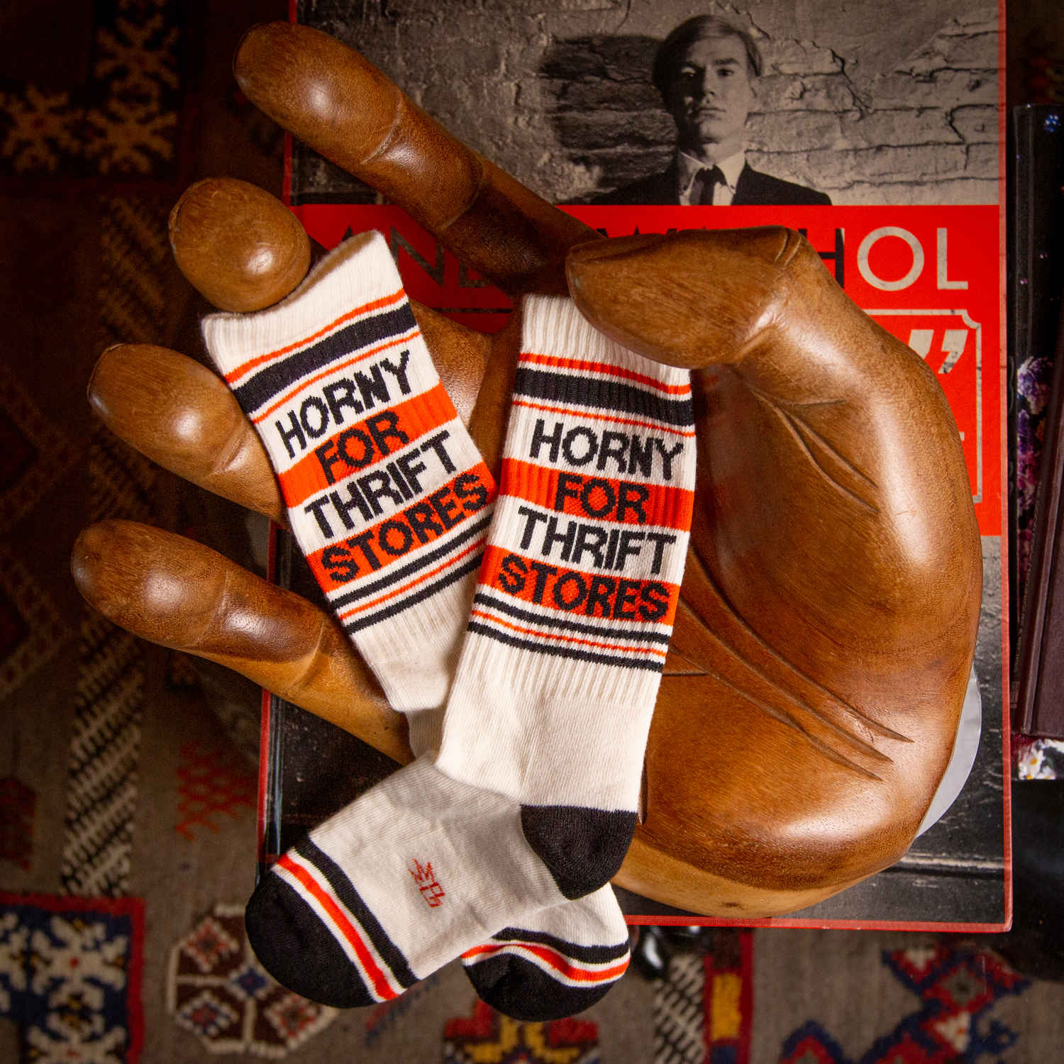 A pair of off-white and red crew socks that read "horny for thrift stores" with the Gumball Poodle logo on the arch.