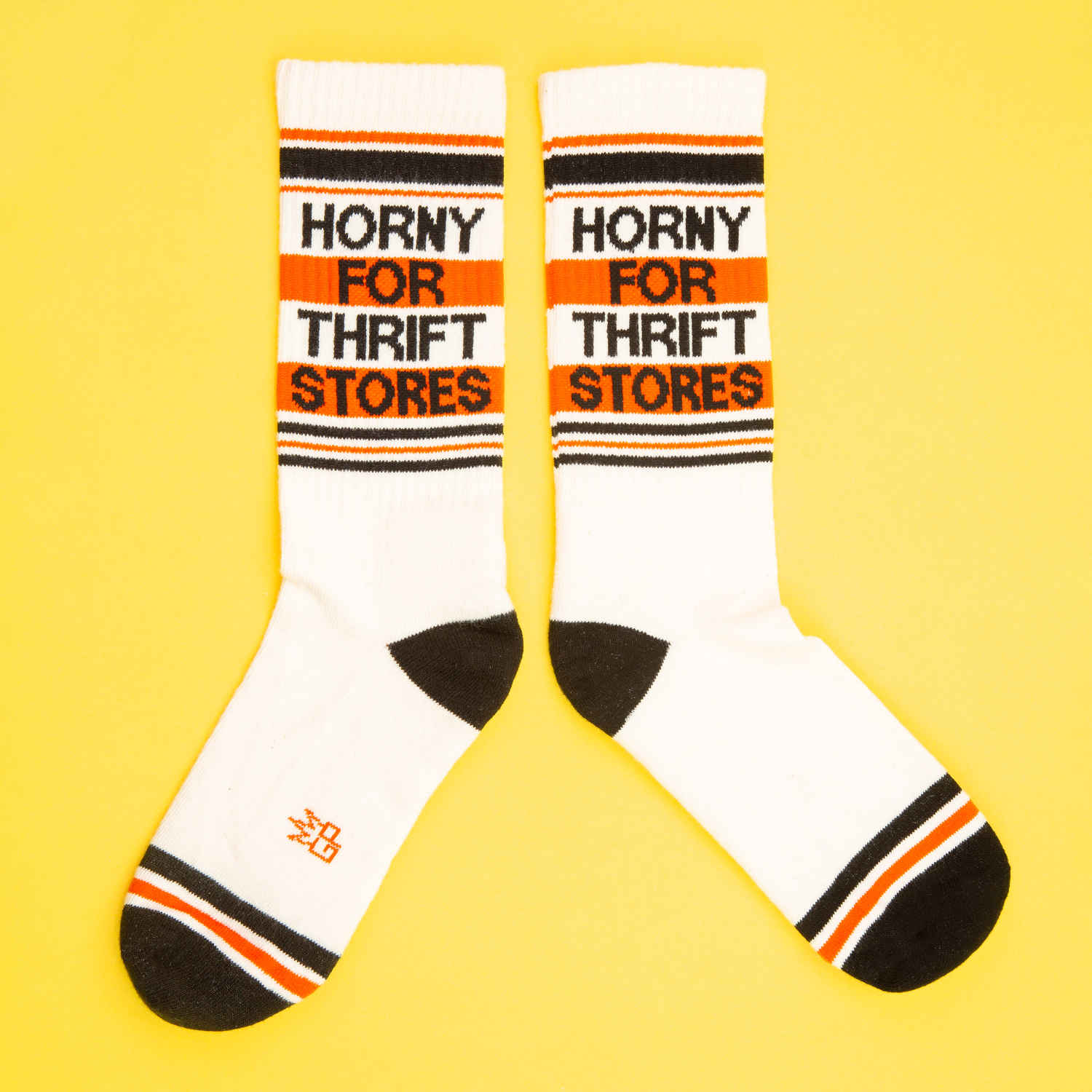 A pair of off-white and red crew socks that read "horny for thrift stores" with the Gumball Poodle logo on the arch.